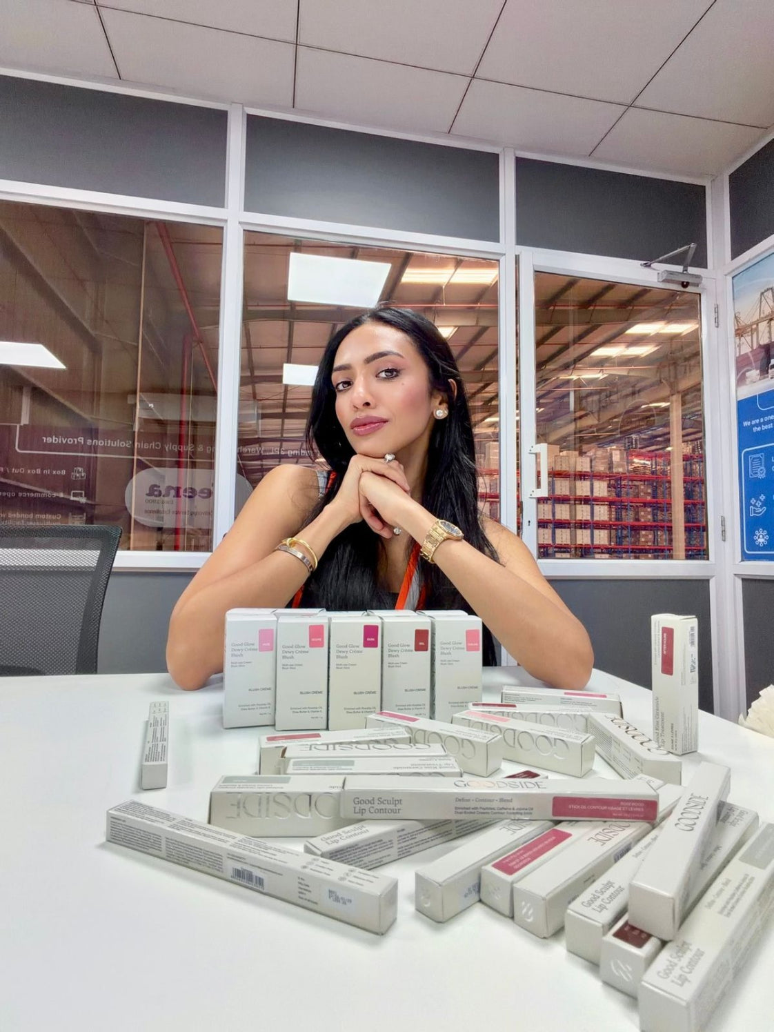 Raveena Mehta (goodsidebeauty) sitting behind a table with multiple boxes of goodside in an indoor setting. - GoodSide